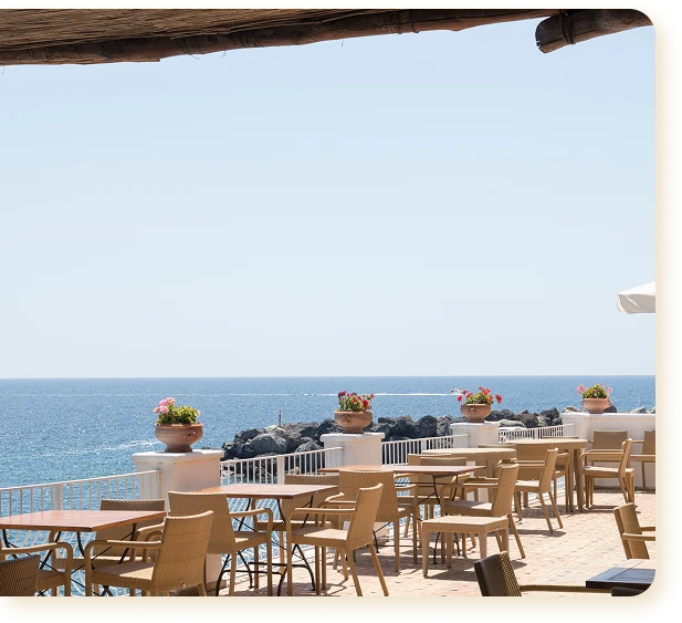 Open-air seaside terrace with wooden tables and wicker chairs on a sunny day